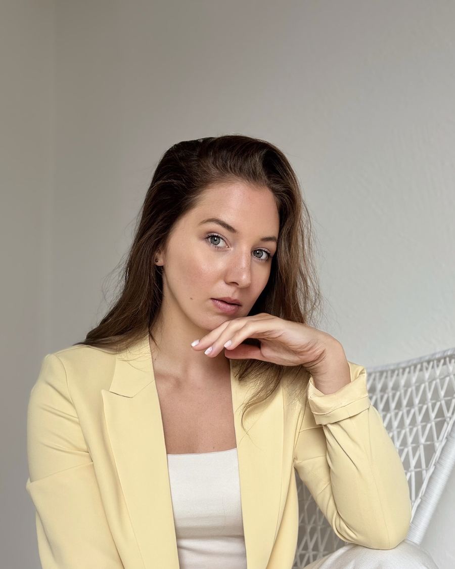Handyfoto einer Frau im gelben Blazer vor einer schlichten Wand, unbearbeitetes Original