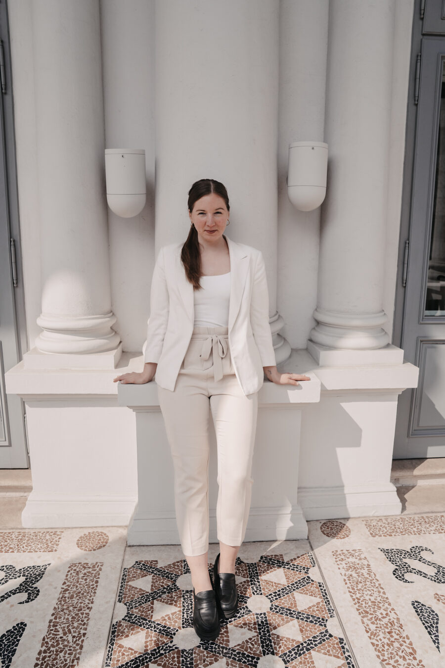 Sarah Bakker im weißen Anzug vor einer weißen Säulenwand, ihre Beige-Zeit