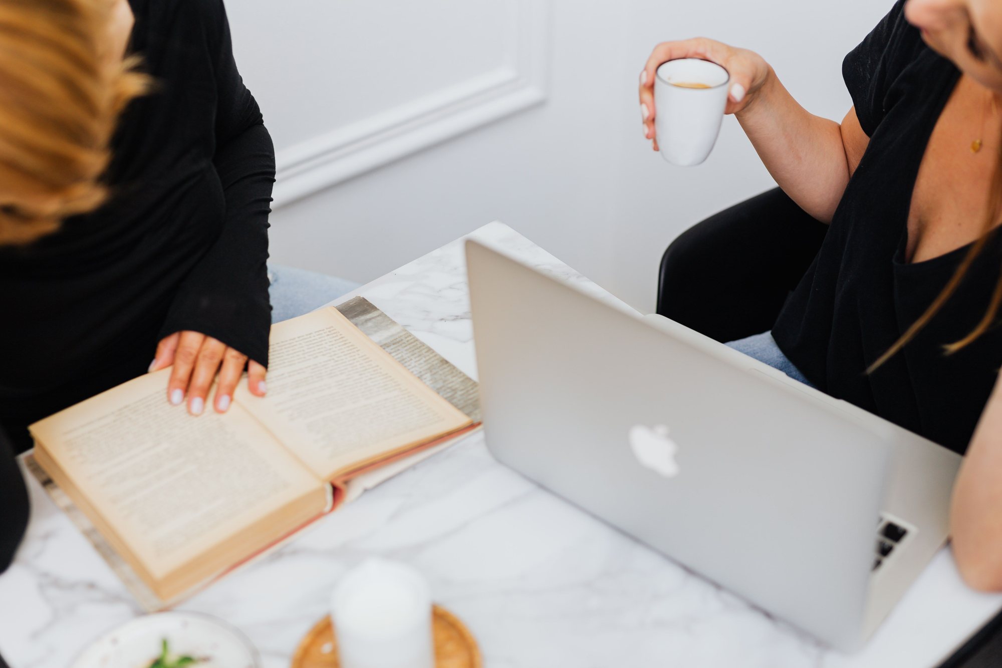 Zwei Frauen im Gespr&auml;ch am Tisch mit Laptop und Buch