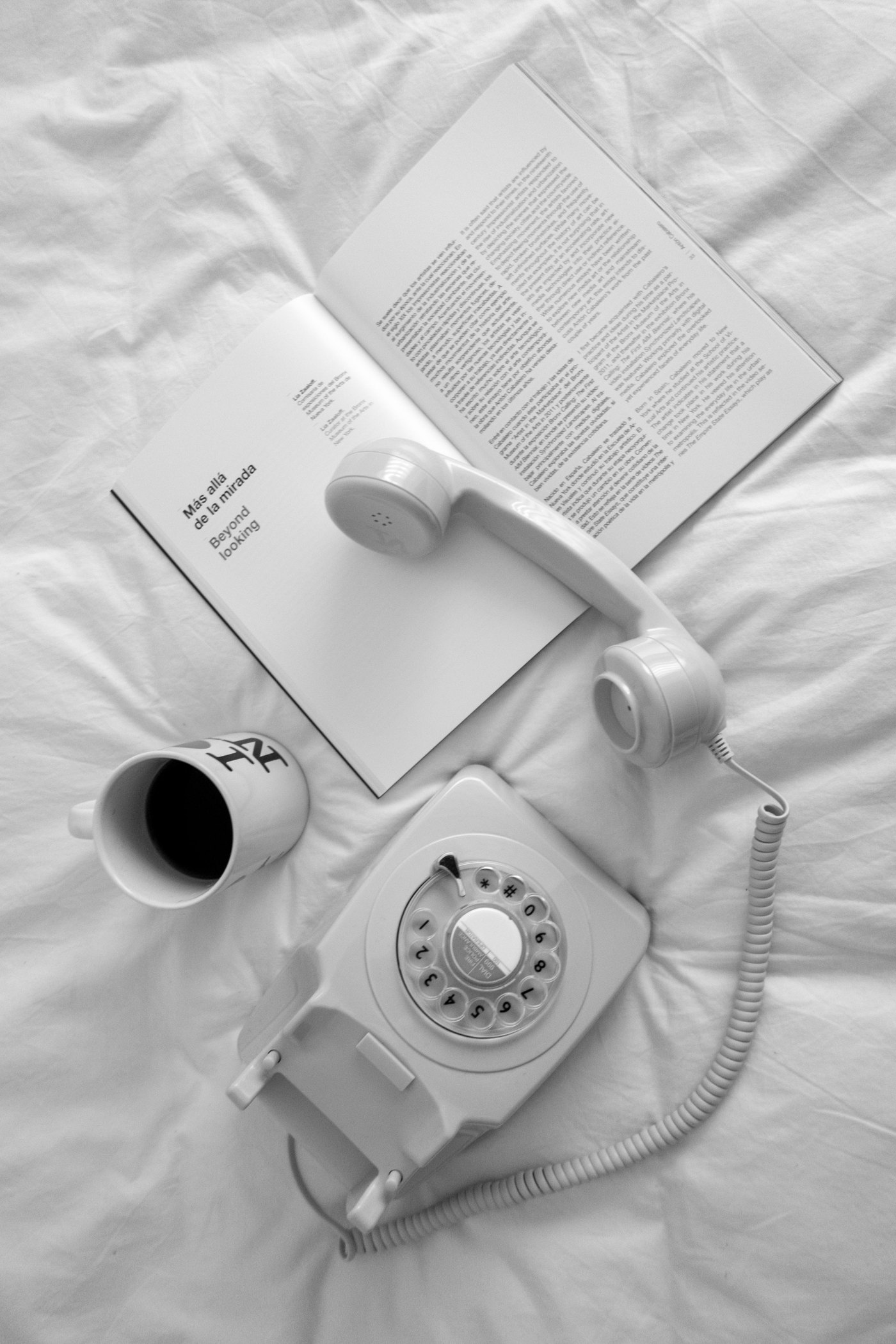 Wei&szlig;es W&auml;hlscheibentelefon, Magazin und Kaffeetasse auf wei&szlig;er Bettw&auml;sche