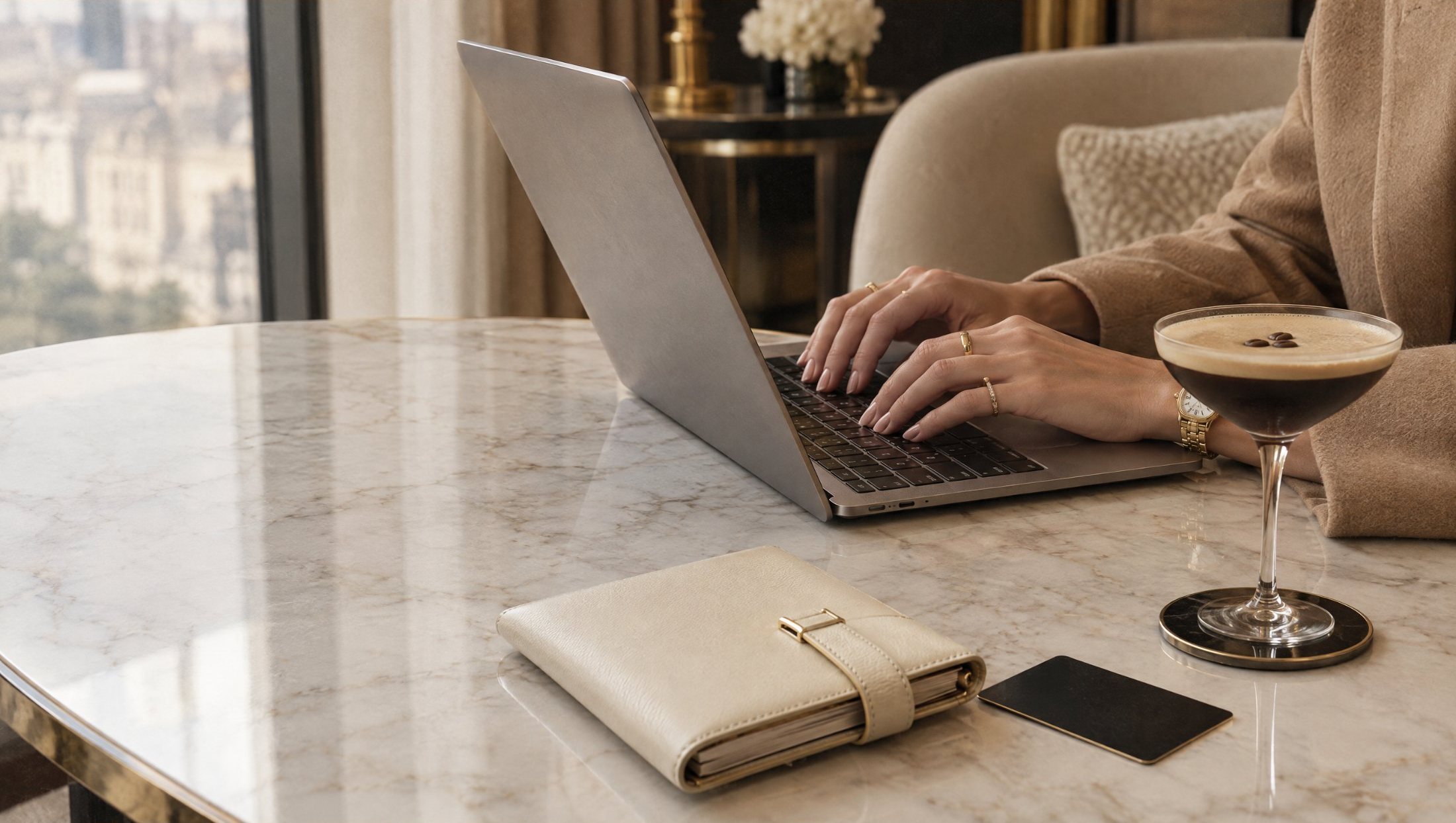 Hände mit Goldschmuck tippen am Laptop auf einem Marmortisch