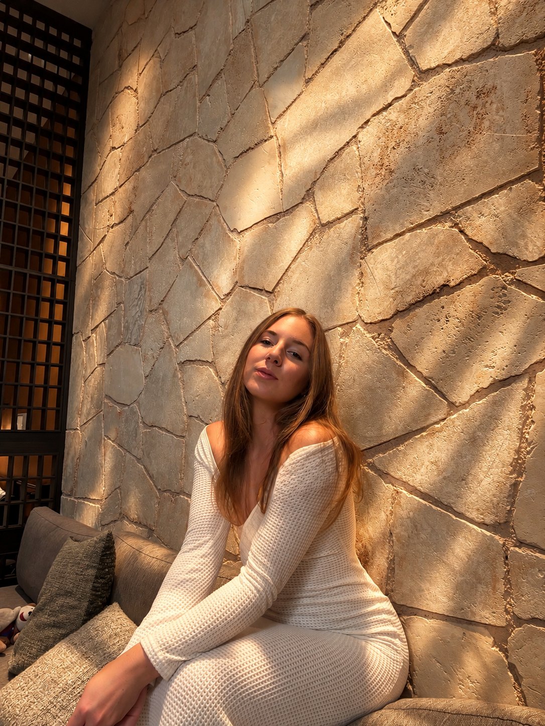 Sarah Bakker sitzt im weißen Strickkleid vor einer Natursteinwand im Abendlicht